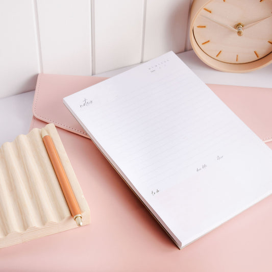An A5 notepad for notes and a to-do list, placed on a folio with a pen beside it, resting on a desk.