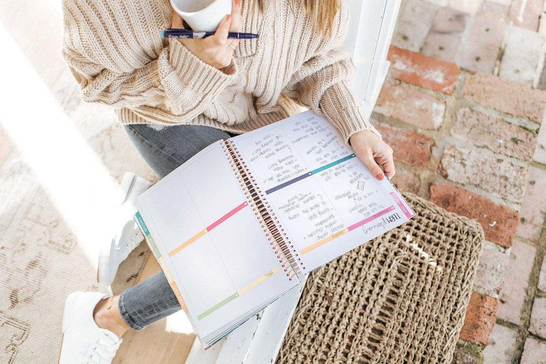 Teacher in a knitted jumper holding a pen and mug with an open planner on her lap, its weekly page filled with handwritten notes