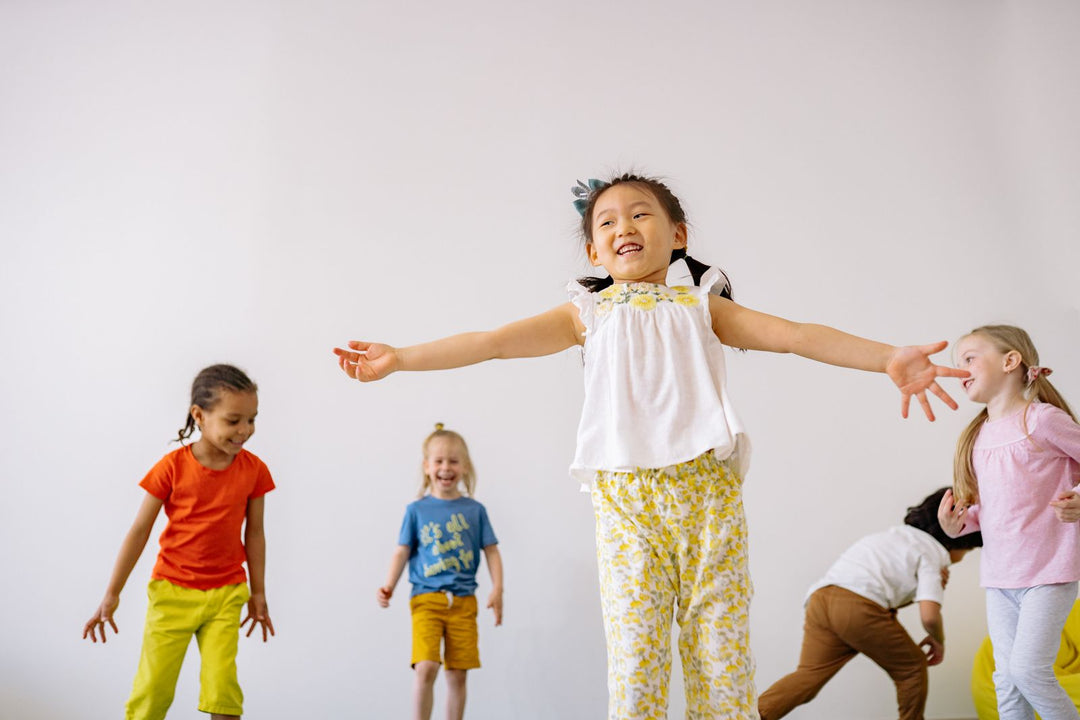 Young children dancing with their arms stretched wide in a bright indoor space