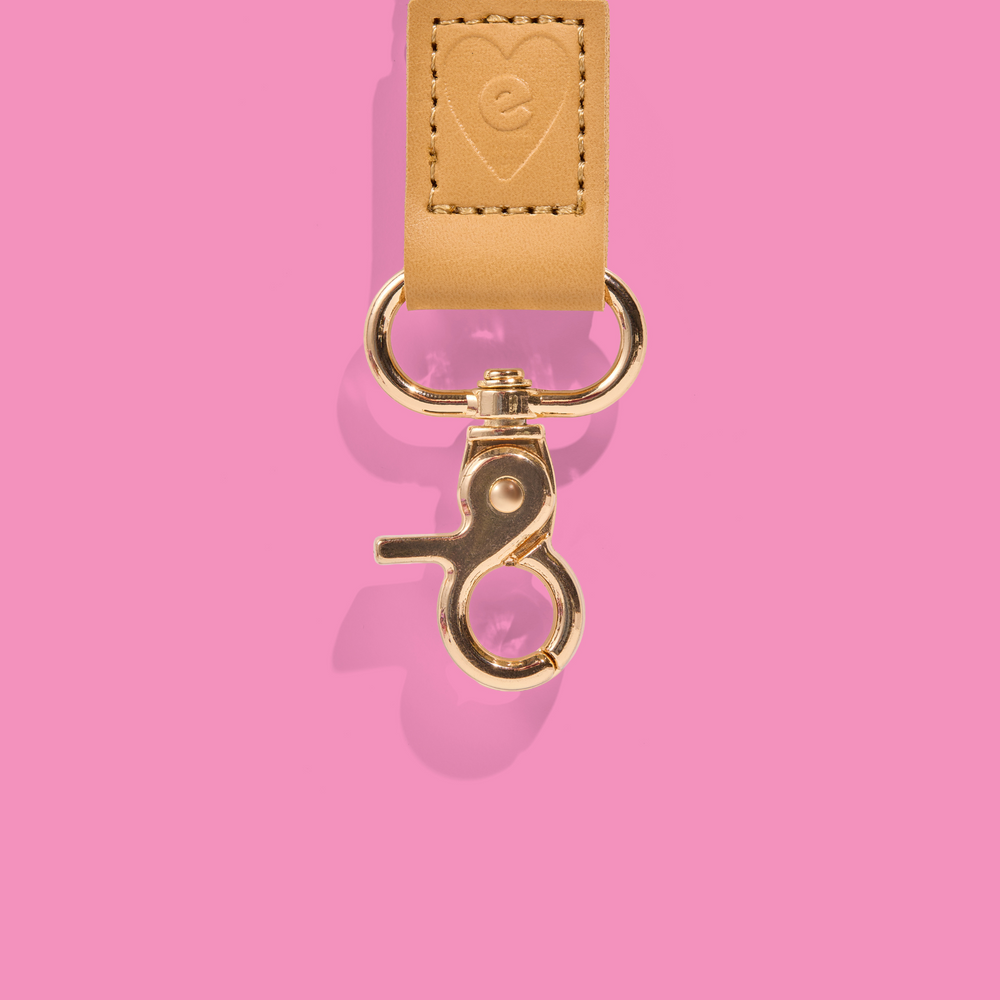Gold clasp and tan leather detail of a teacher lanyard embossed with the Mrs Edgar logo, set against a pink background.
