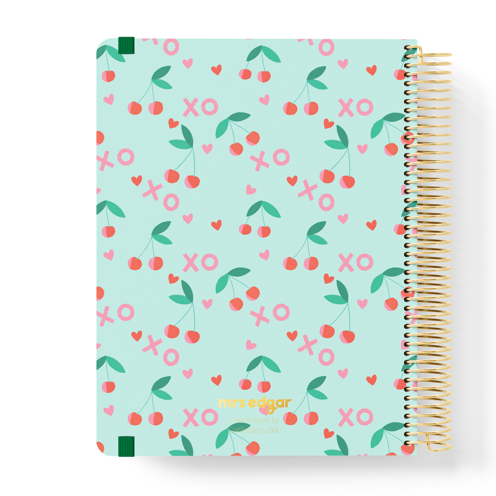 2026 teacher planner with a mint green cover featuring cherry illustrations, pink XOs, and hearts in a playful pattern