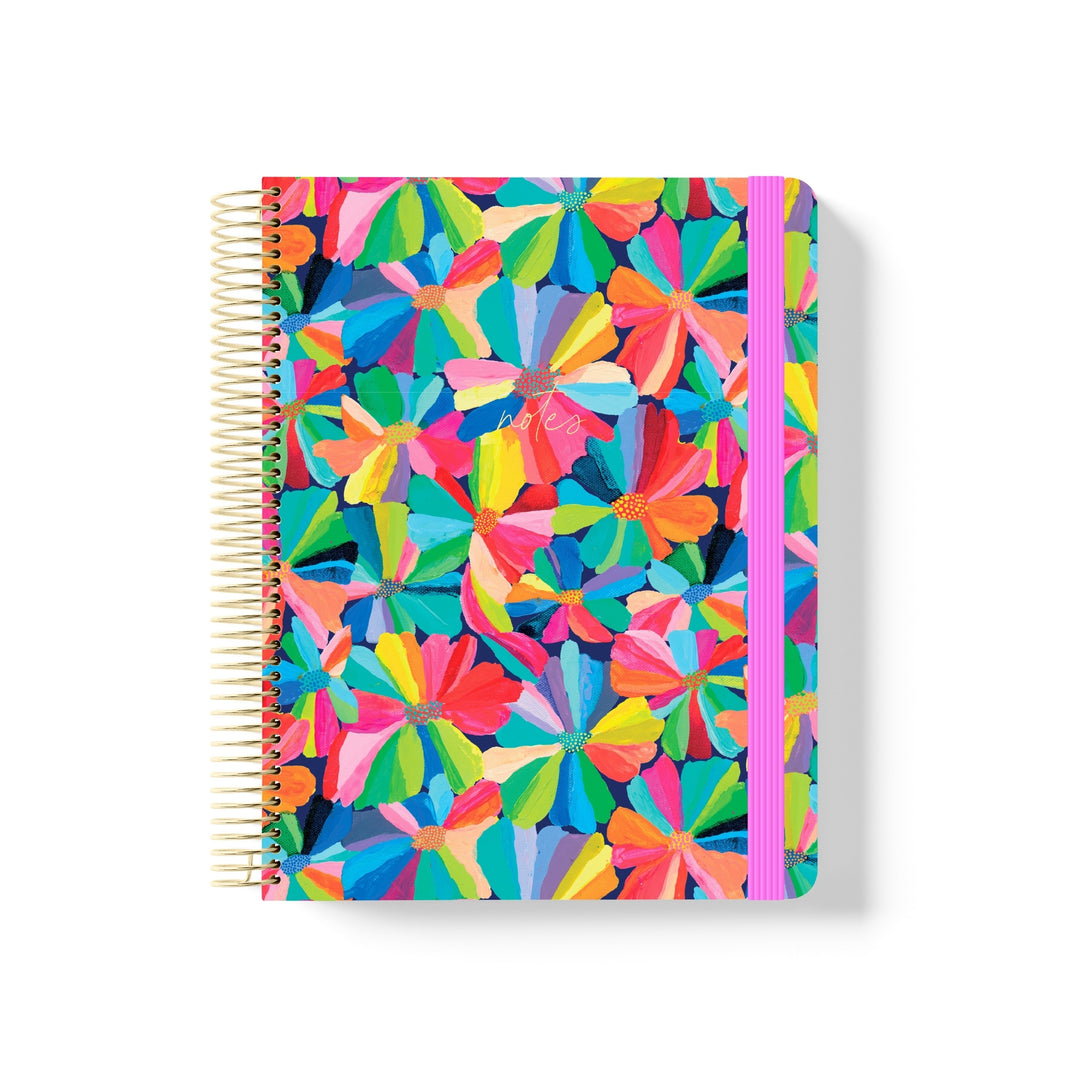 Coiled notebook with bold multicolour floral pattern, gold spiral binding, pink elastic band, and white “notes” text on the cover.