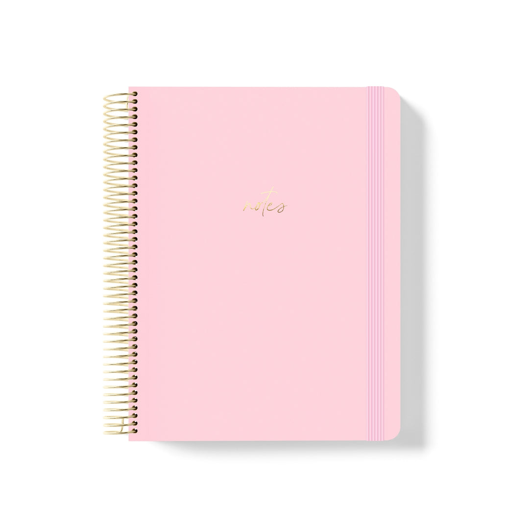 Blush pink coiled notebook with gold spiral binding, matching elastic band, and metallic gold “notes” text centred on cover.