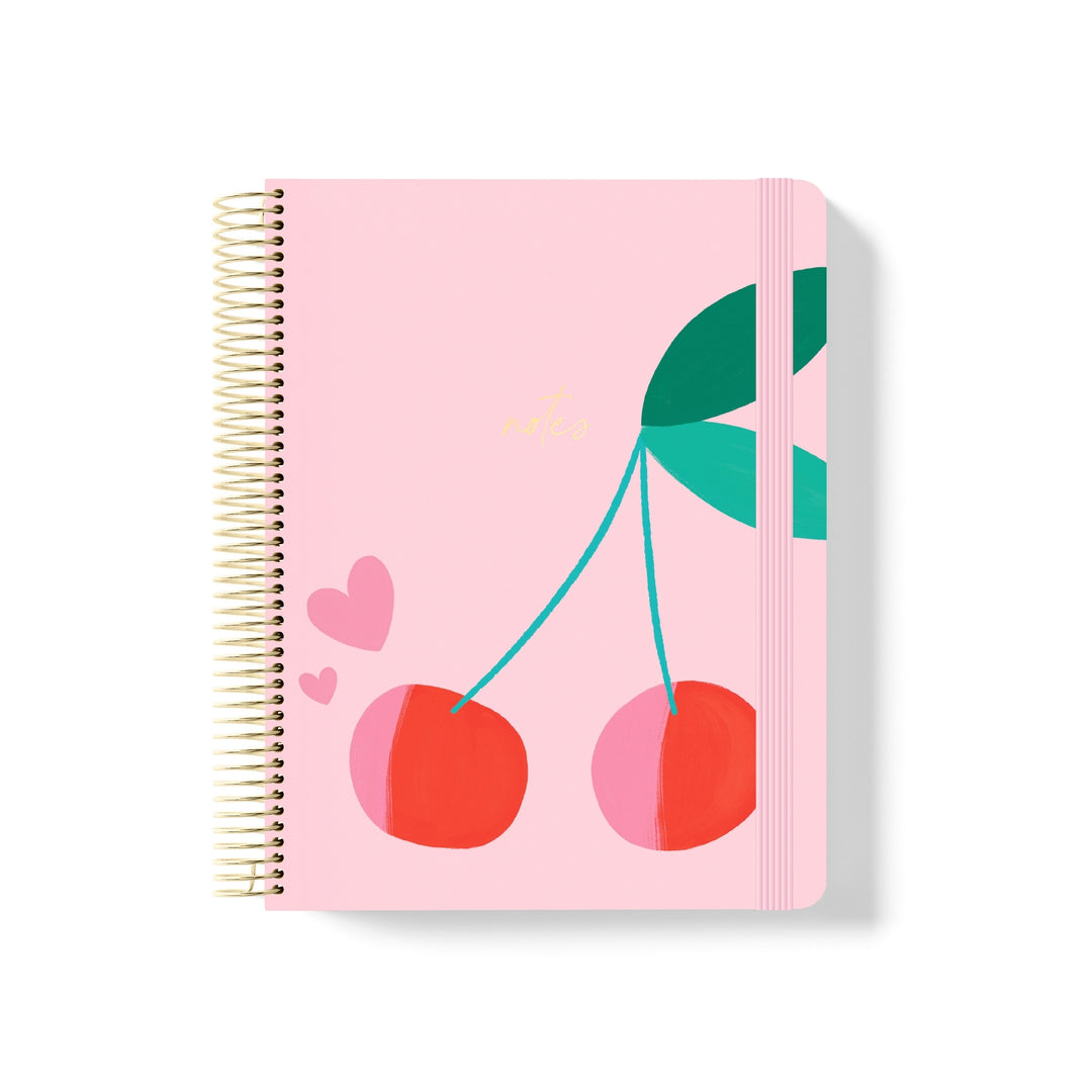 Pink coiled notebook with gold spiral, cherry illustration, pink hearts, and gold “notes” text on the front with matching elastic band.