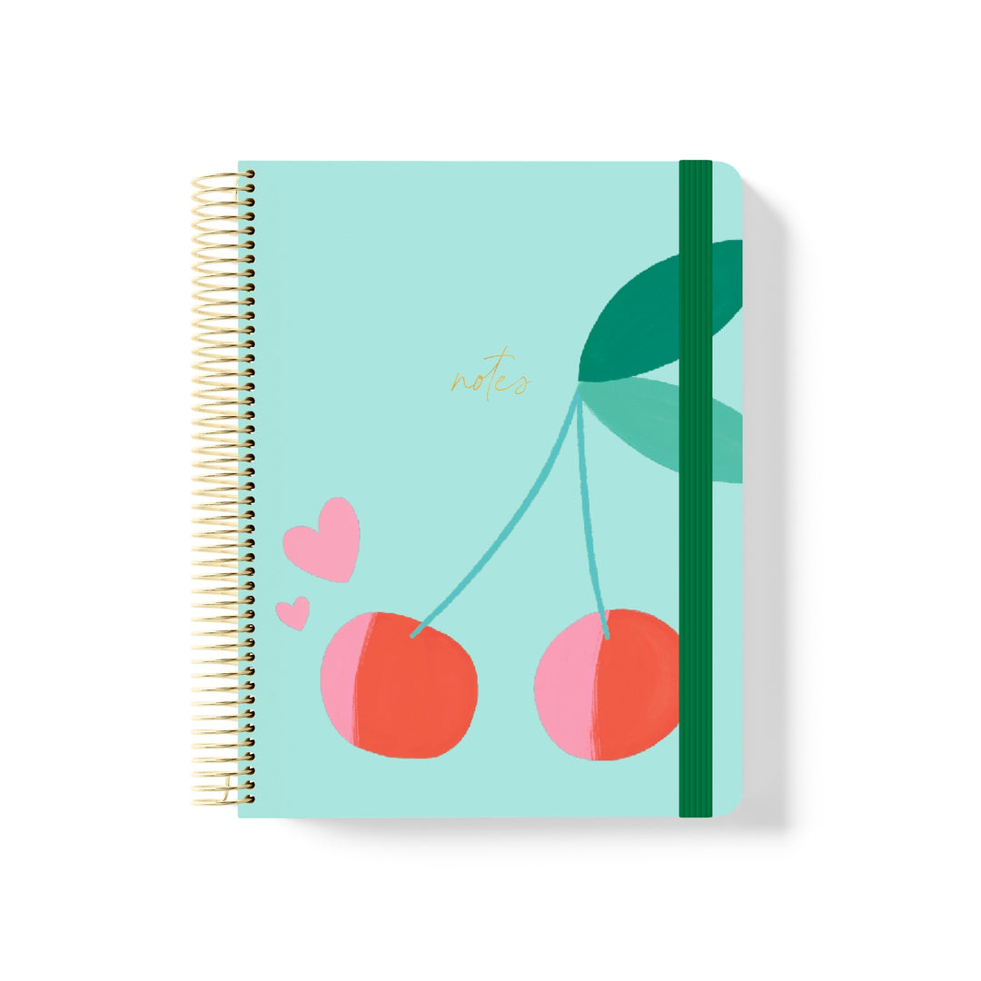 Mint green coiled notebook with gold spiral, cherry and heart illustration, dark green elastic band, and gold “notes” text.