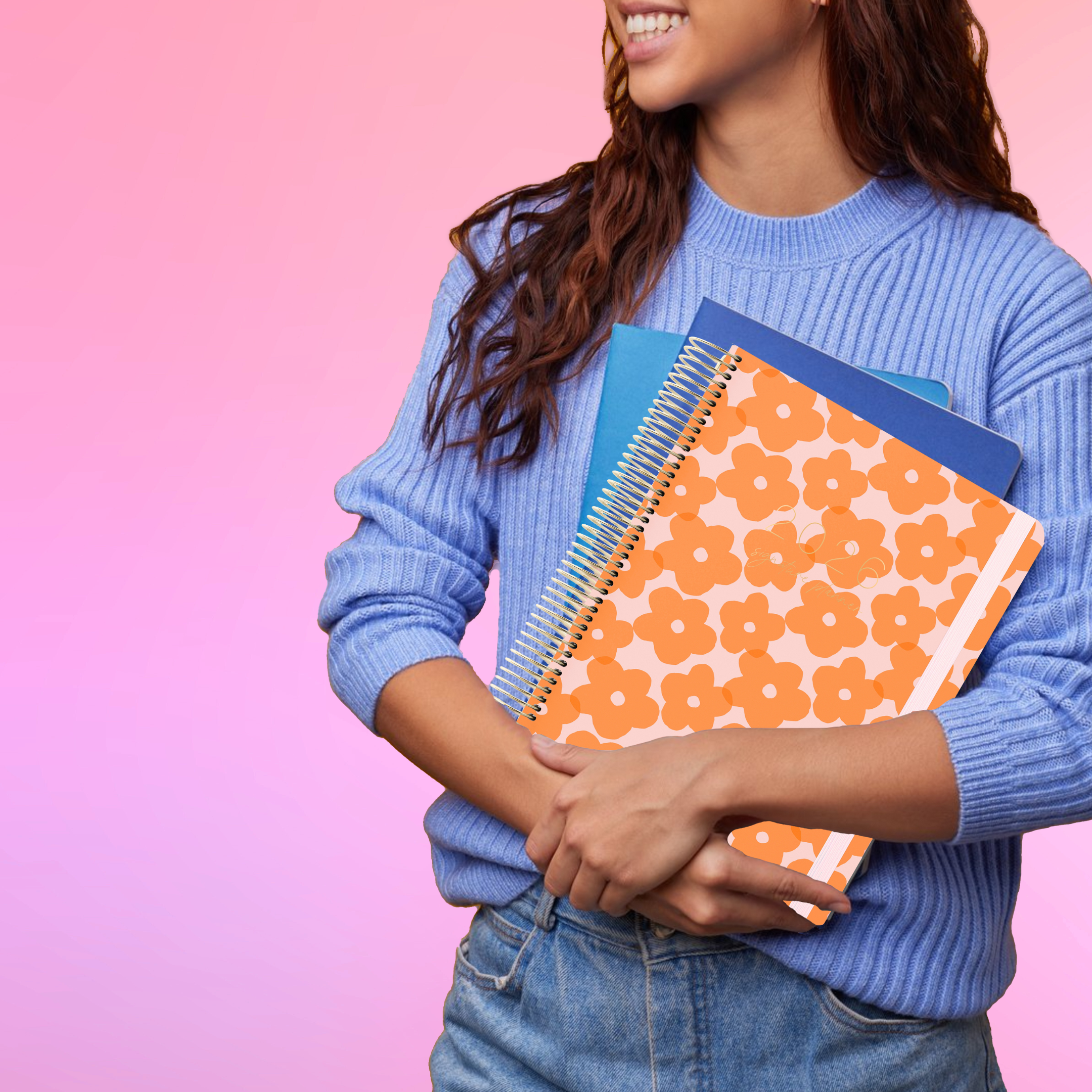 Smiling woman in a blue sweater holds the 2026 teacher planner with orange flowers on the cover.