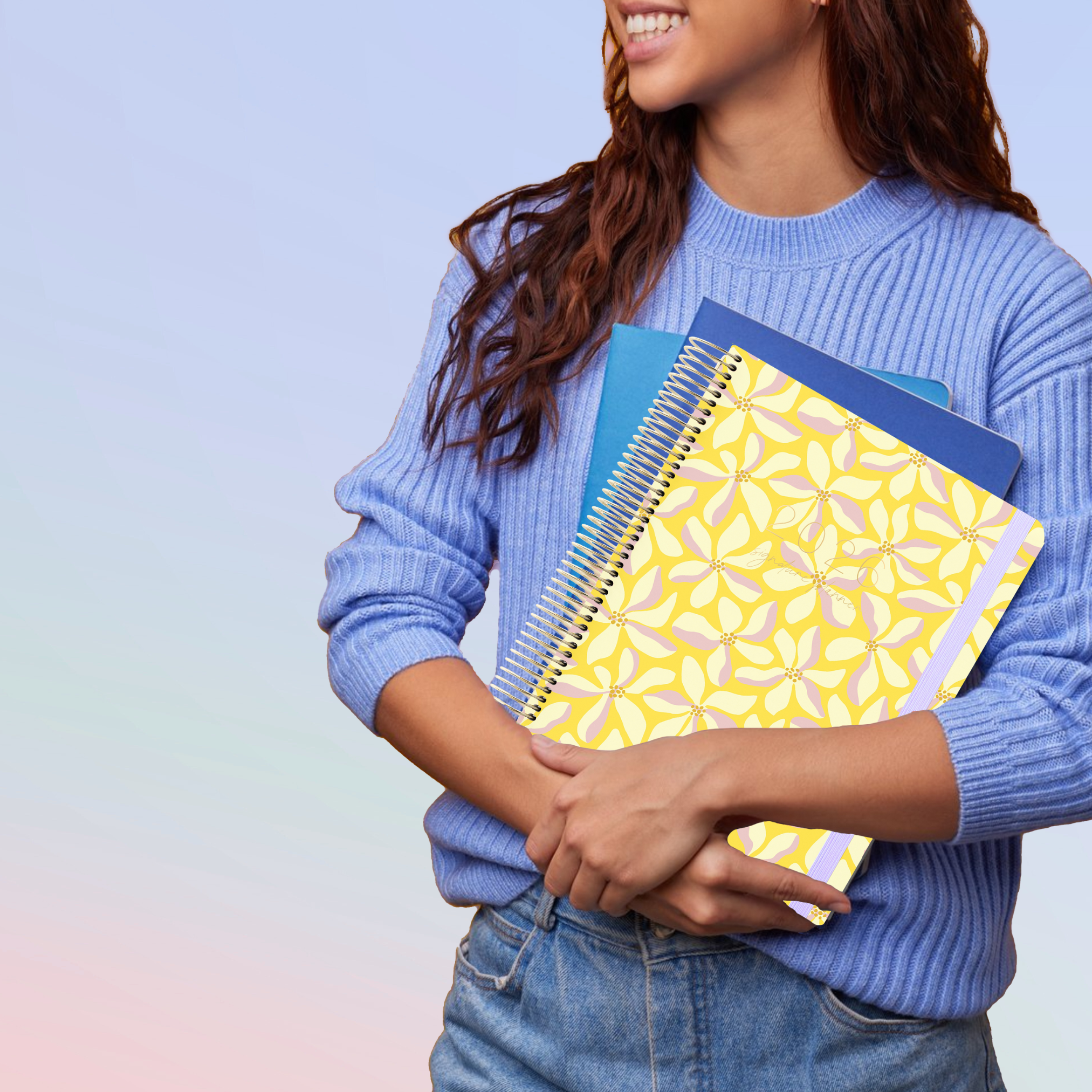 Woman in blue sweater holding 2026 yellow floral planner with gold coil and lavender elastic strap.