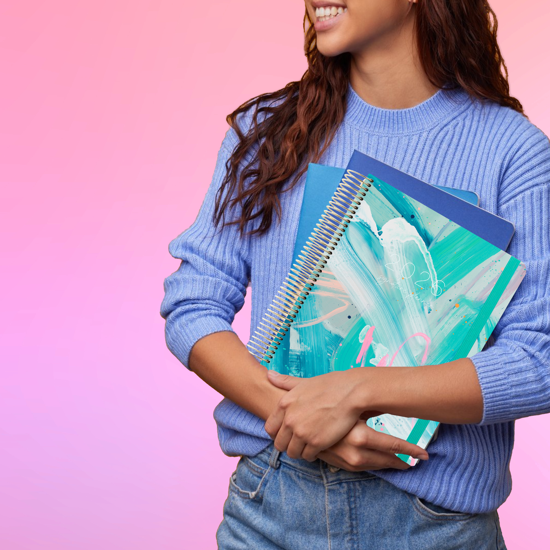 Smiling woman in a blue sweater holds the 2026 teacher planner with a modern blue artwork on the cover.
