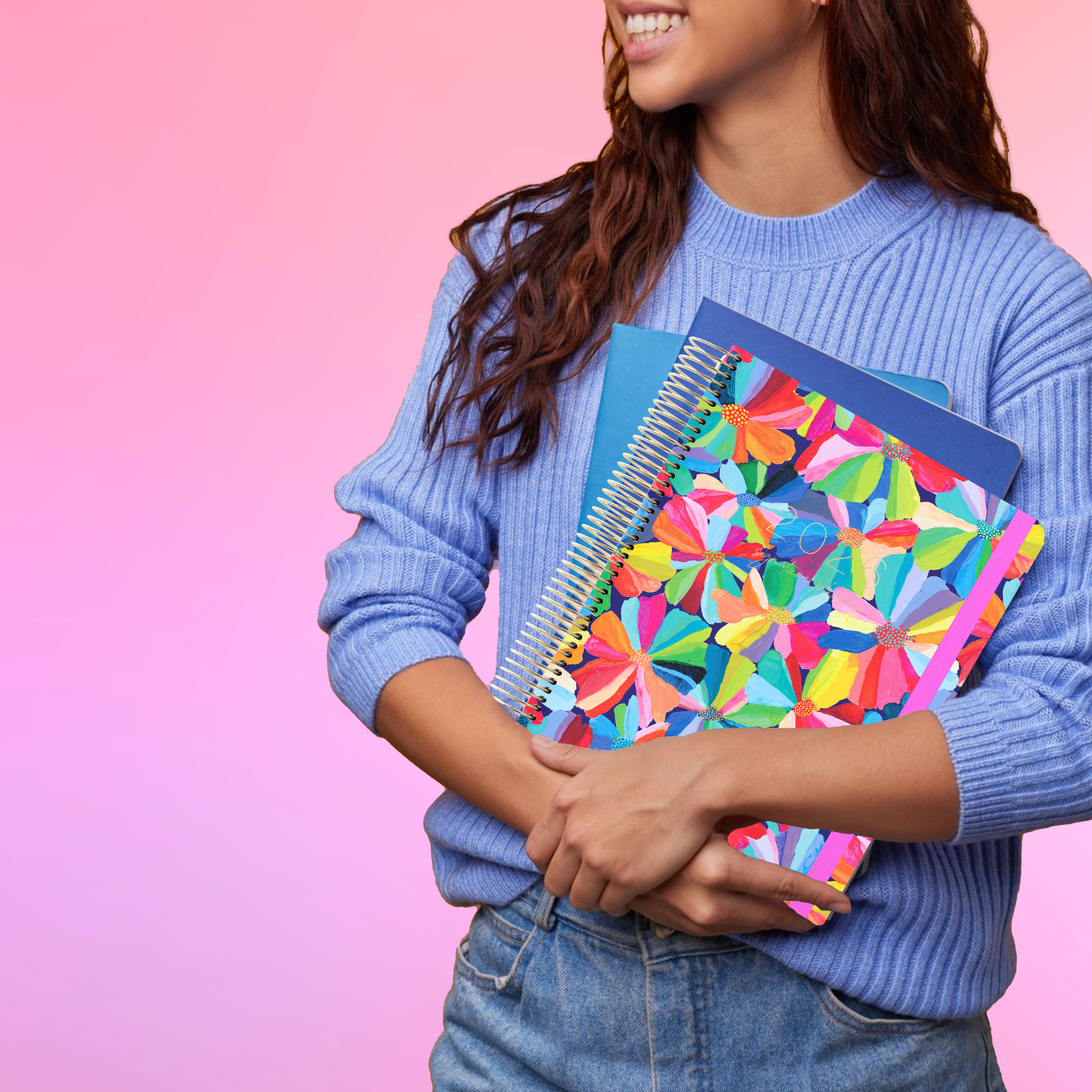 Smiling woman in a blue sweater holds the 2026 teacher planner with bright and colourful flowers on the cover.