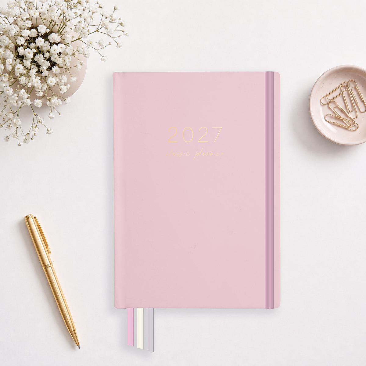 2027 Blush Classic Weekly Teacher Planner flat lay with soft pink cover and gold foil, styled with baby's breath and a gold pen