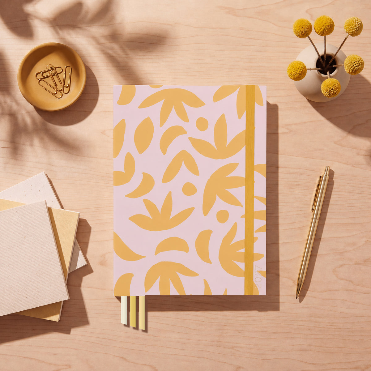 2027 Sunburst Golden Slimline Classic Teacher Planner flat lay with yellow leaf pattern on blush cover, styled with billy buttons and a gold pen