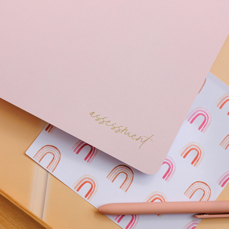Placed on a decorative surface, the blush assessment journal showcases its sleek design and elegant features.