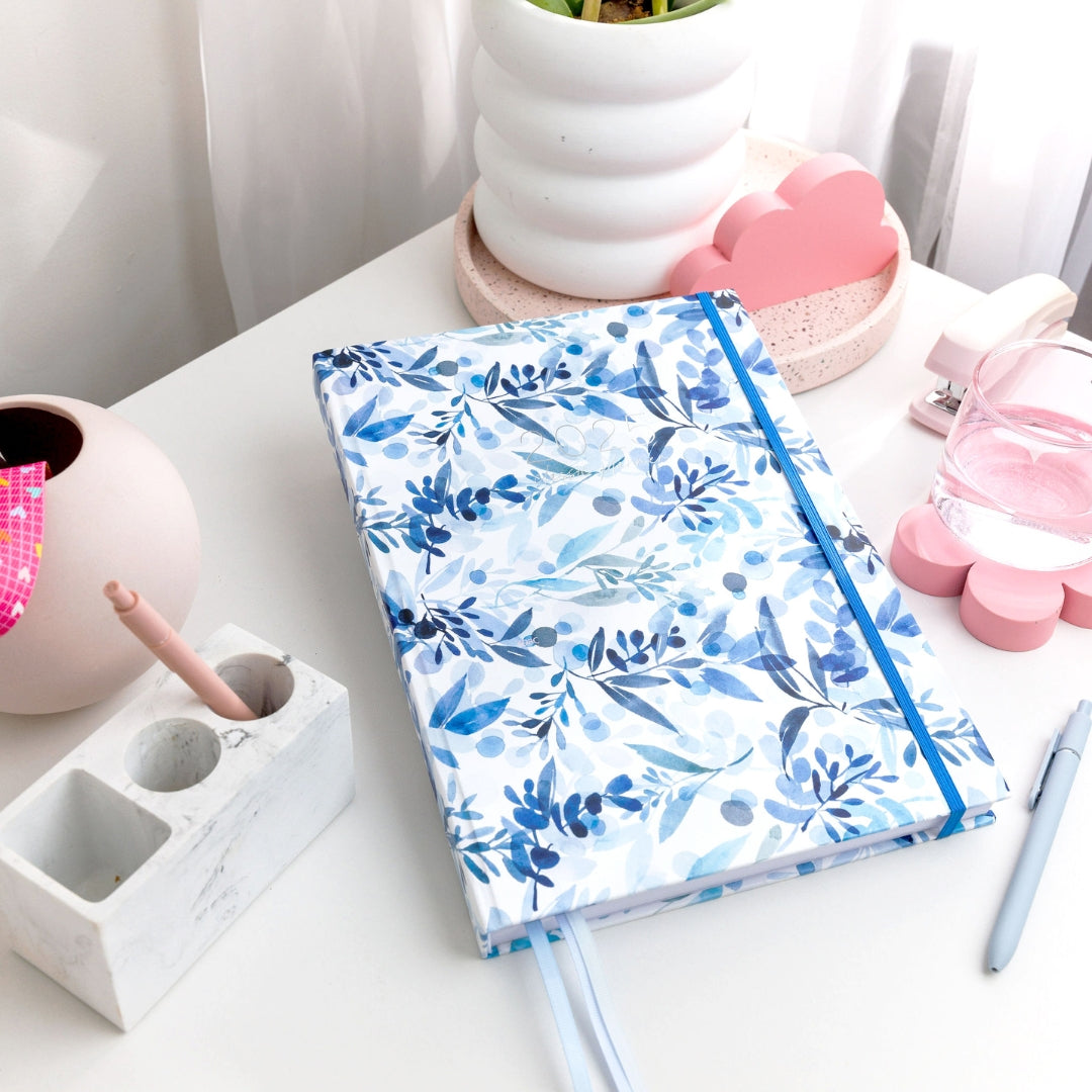 2025 Classic Weekly Teacher Planner named Snow Drift, on a desk, featuring blue and white flora artwork in cool colours.