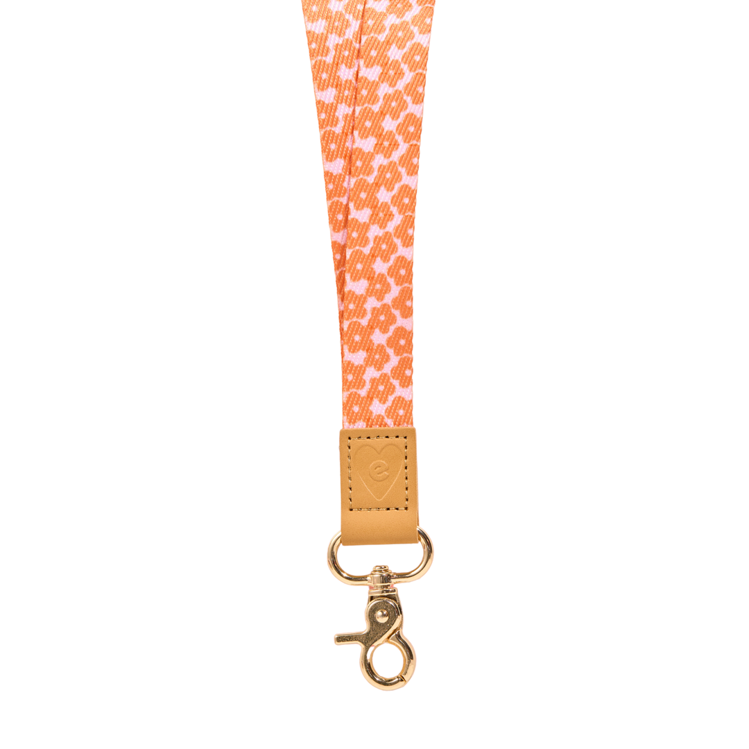 Orange floral fabric lanyard with tan leather tab and gold clasp, featuring embossed heart logo detail, isolated on a clean white background