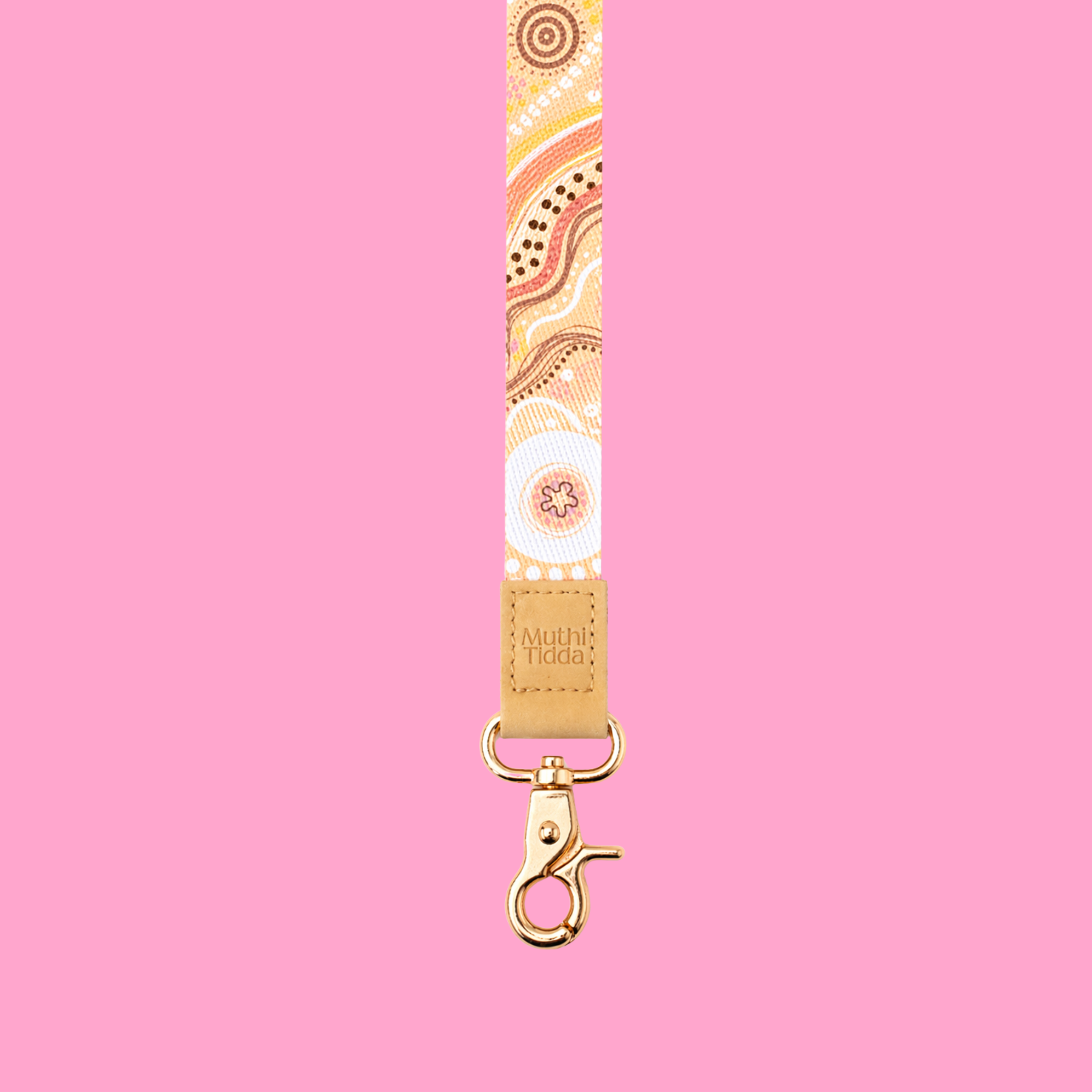 Cream and pastel Indigenous-inspired patterned lanyard with tan leather logo detail and gold clasp displayed against a soft pink background.