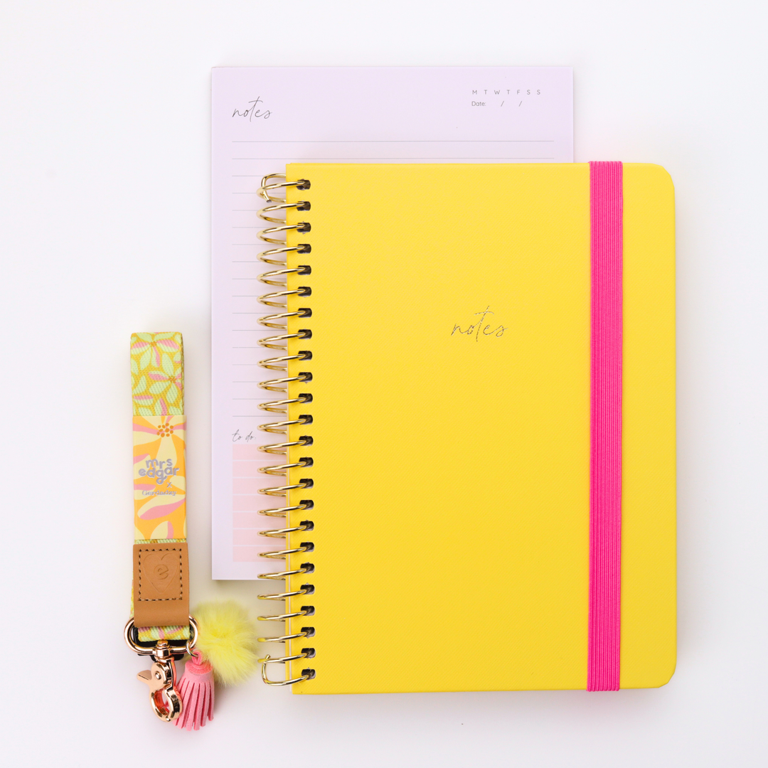 Bright yellow A5 teacher notebook with pink elastic band styled with matching floral lanyard and notepad on a clean white background