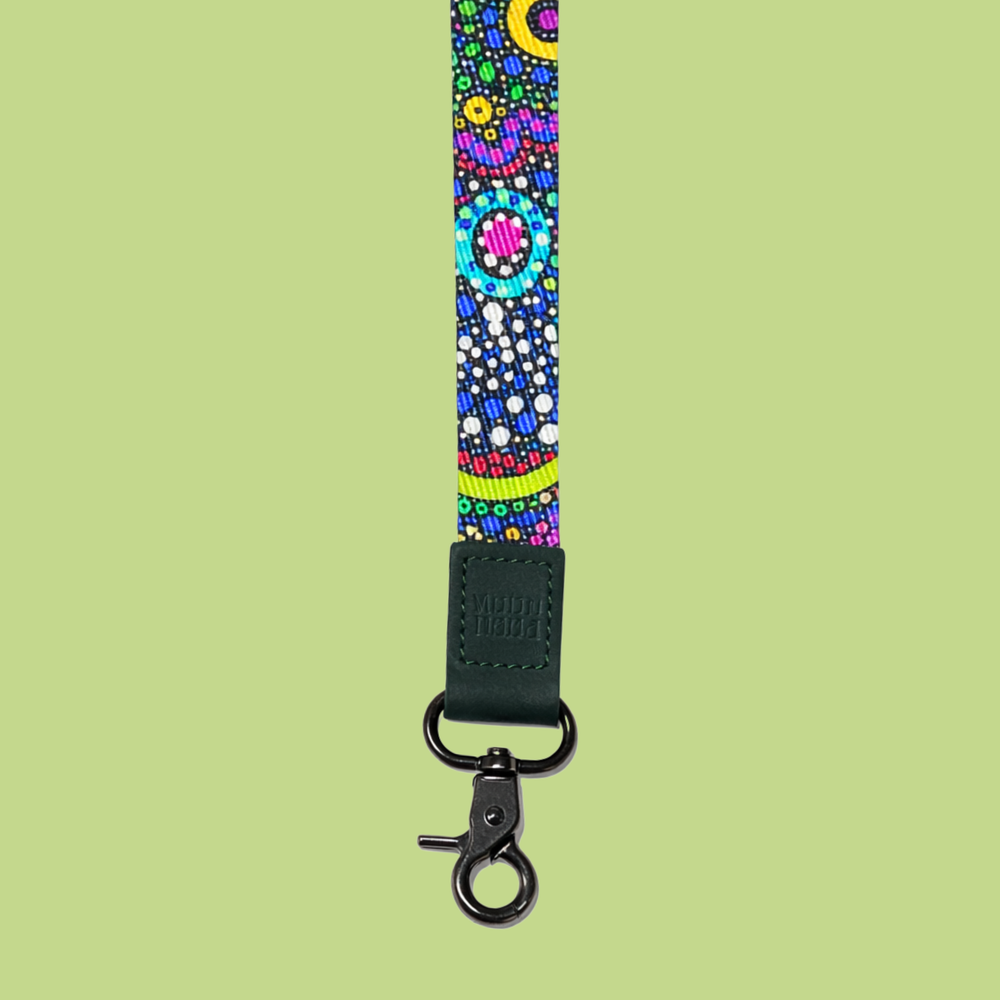 Pink festive lanyard with holiday characters including reindeer and Santa, finished with a tan leather logo patch and gold hardware on a soft green background.