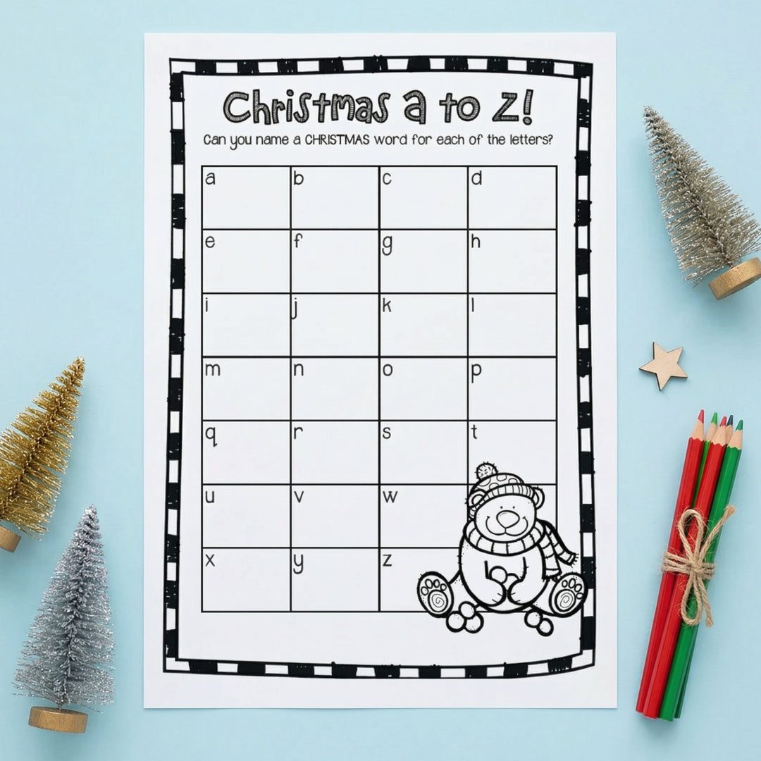 Black-and-white “Christmas A to Z!” printable worksheet asking students to write a Christmas-related word for each letter of the alphabet. The page features a grid labeled with lowercase letters a–z and a cartoon teddy bear in winter clothing at the bottom. The worksheet is displayed on a light blue background with small Christmas trees, a wooden star, and colored pencils.