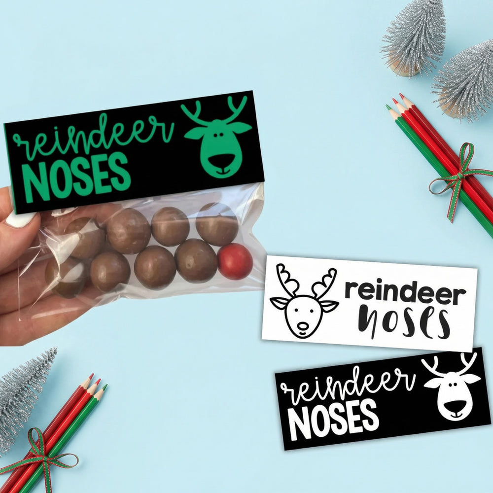 Printable “Reindeer Noses” bag topper labels displayed with a small treat bag of chocolate balls and a red candy, styled on a blue background with Christmas decorations and coloured pencils.