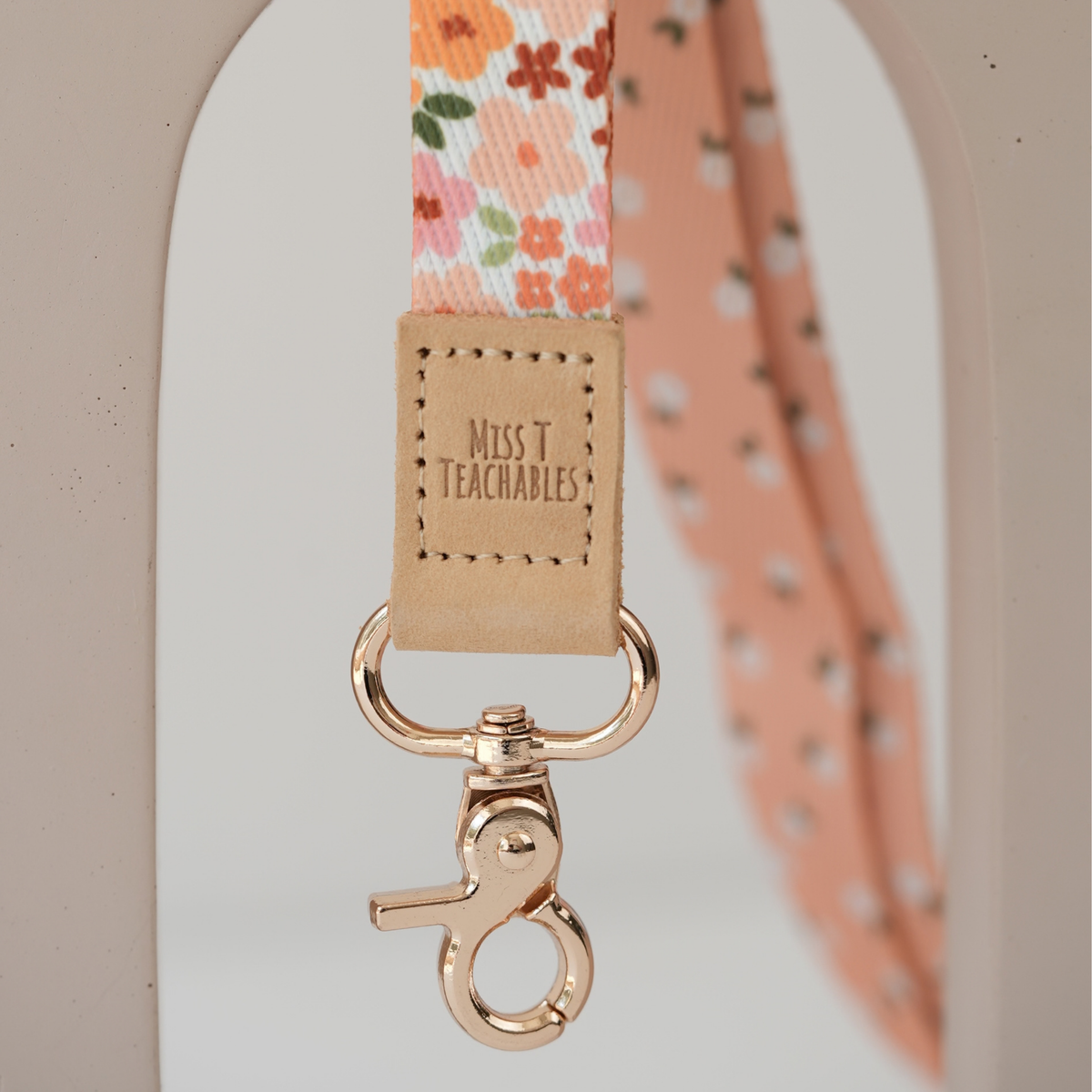 Close up of Boho Ditsy Floral lanyard clasp, embossed Miss T Teachables tan tab and gold swivel clasp