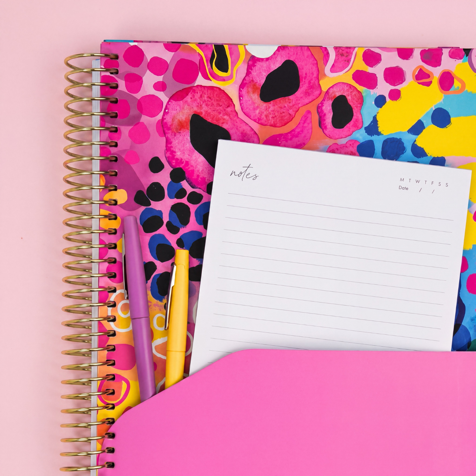 2027 Boom Planner showing pink pocket sleeve with notes page and pens, gold coil on a pink background.