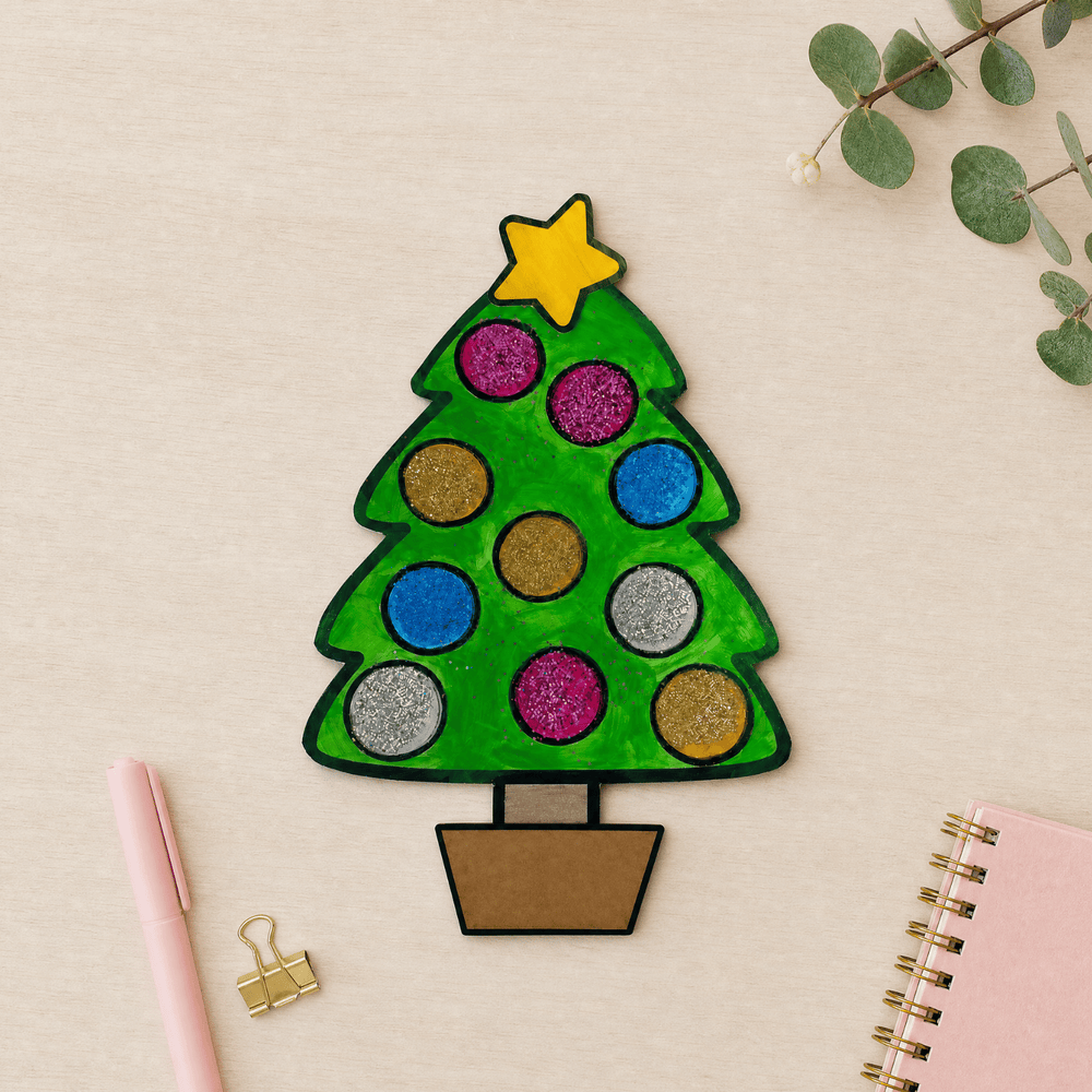 Completed Christmas tree craftivity with glitter ornament circles and yellow star, displayed with pink stationery.