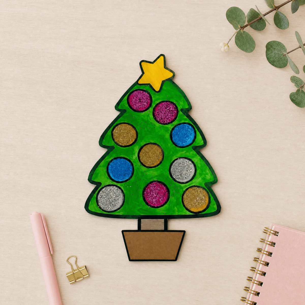 Completed Christmas tree craftivity with glitter ornament circles and yellow star, displayed with pink stationery.