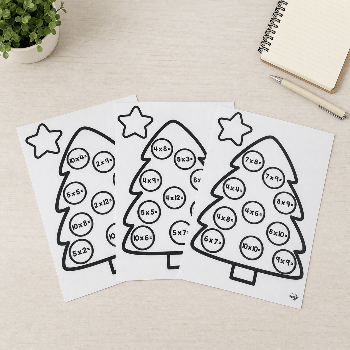 The three mixed revision Christmas tree sheets fanned out on a desk, each printed in black and white with ten multiplication facts in bauble circles and a blank star at the top.