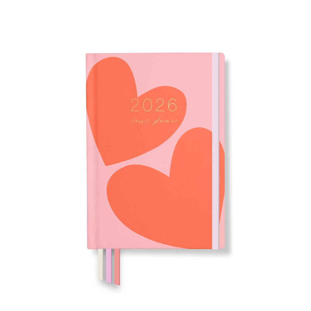 2026 classic planner front cover featuring two bold red-orange hearts on a soft pink background with ribbon markers and elastic closure.