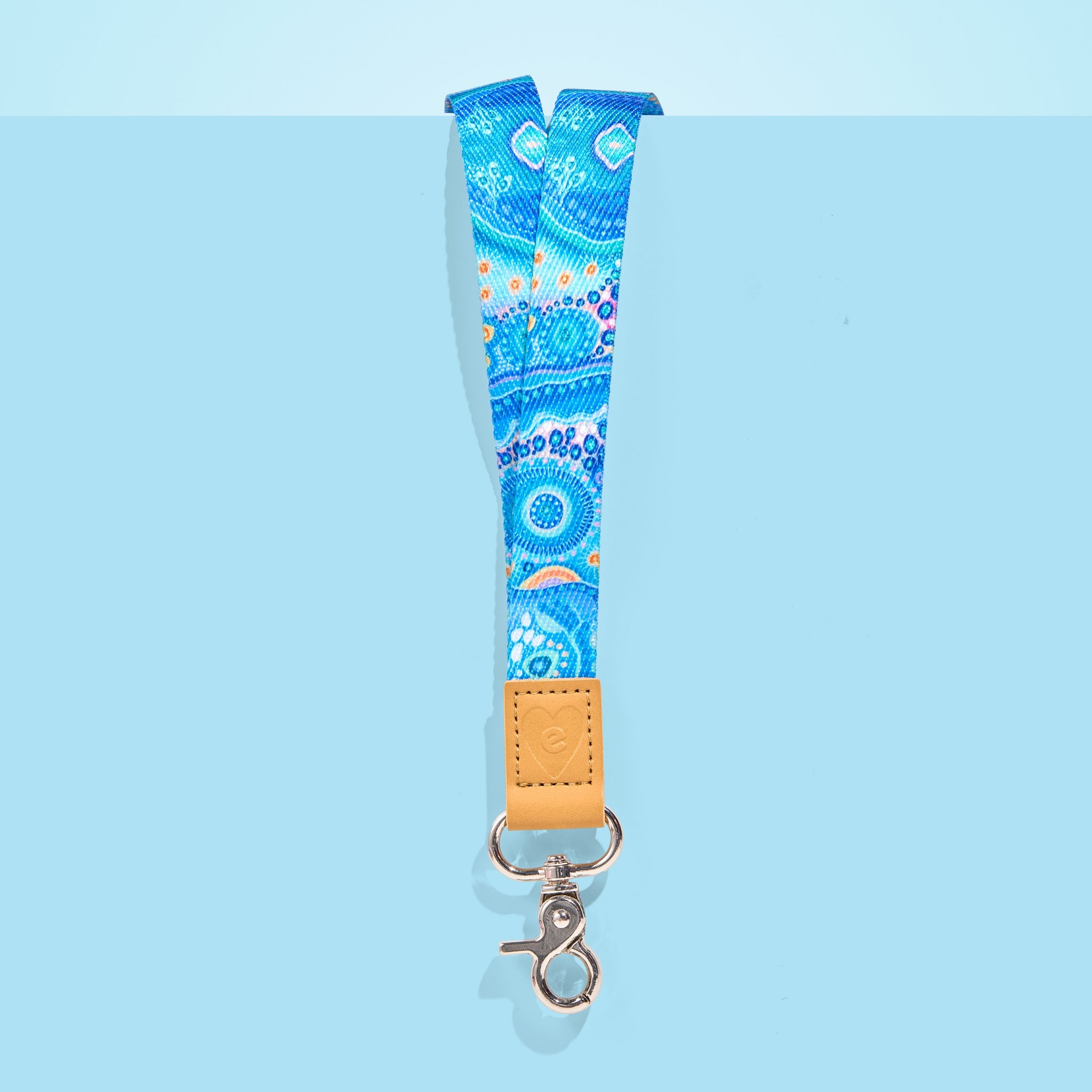 Blue Aboriginal art teacher lanyard with tan leather accent and silver clasp, displayed on a light blue background.