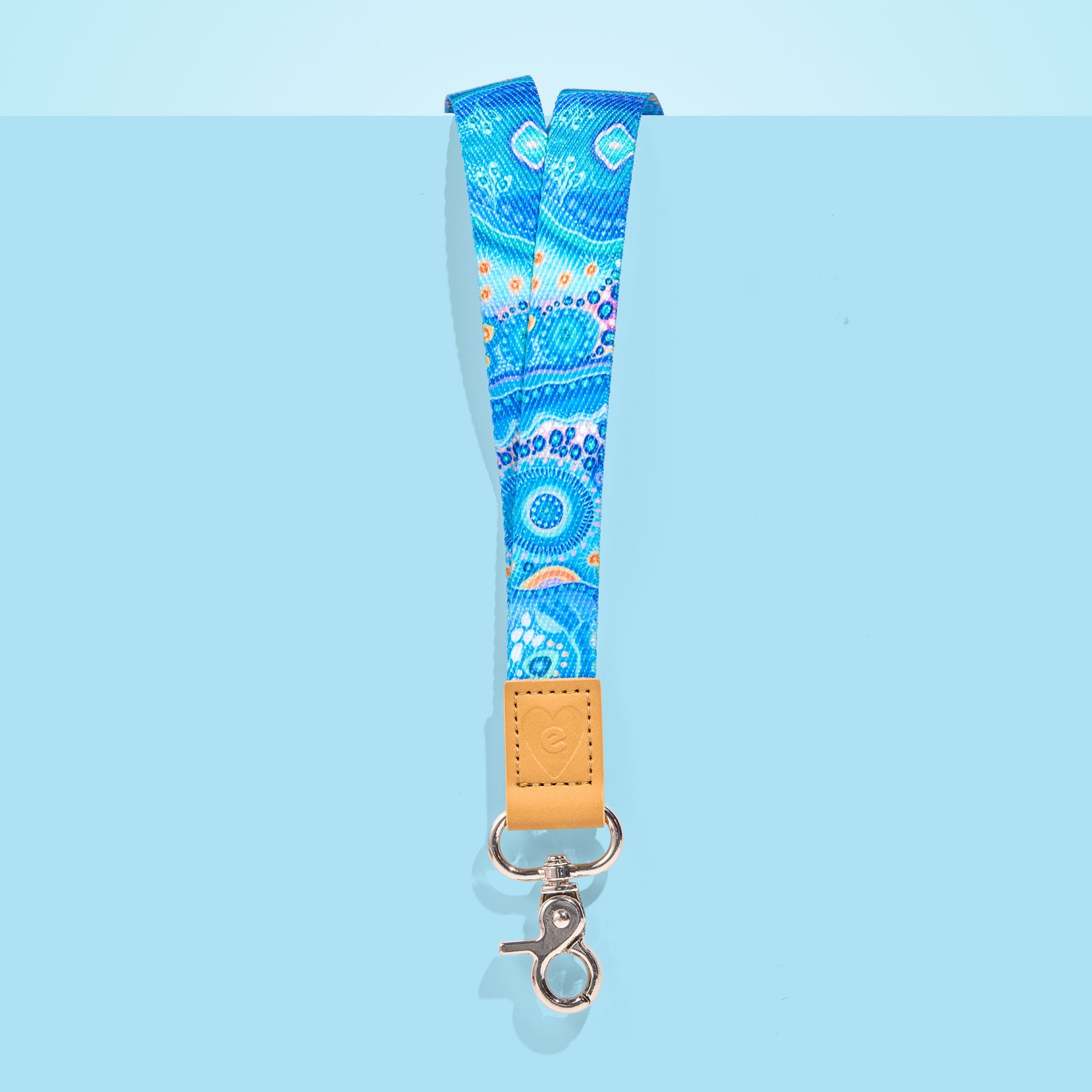 Blue Aboriginal art teacher lanyard with tan leather accent and silver clasp, displayed on a light blue background.