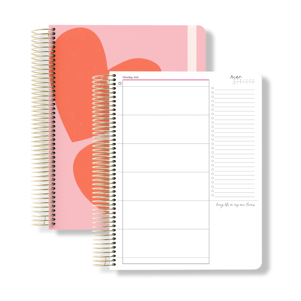 Flat lay of the 2026 daily teacher planner with oversized red heart shapes on a pink cover, shown beside an open daily layout.
