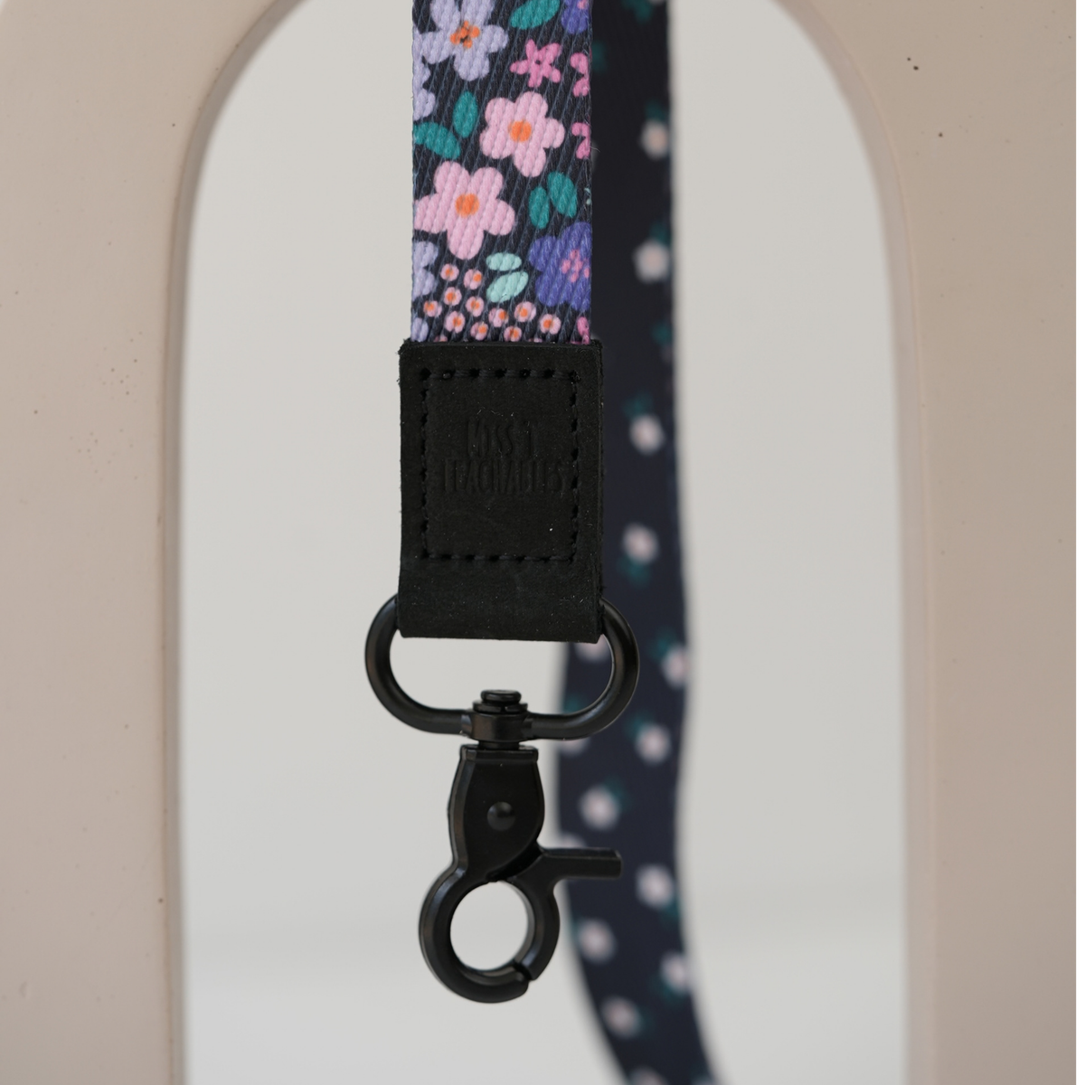 Close up of Dark Ditsy Floral lanyard clasp, embossed Miss T Teachables black tab and matte black swivel clasp