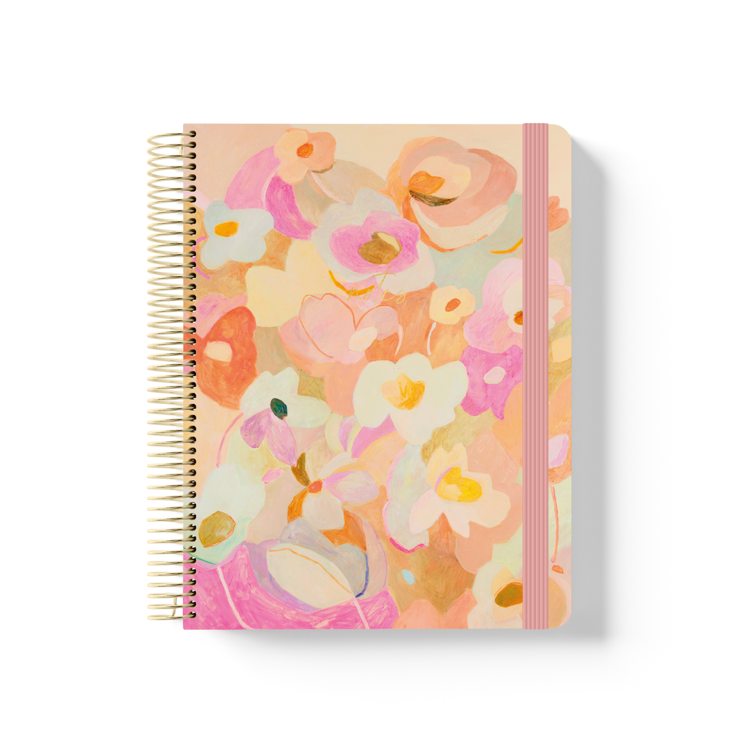 Love Fool spiral notebook with painted floral artwork in pink, peach and cream, gold coil binding, and pink elastic closure.