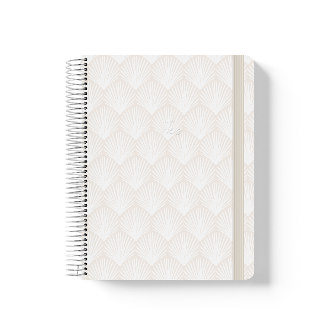 Shells spiral notebook with a repeating fan shell pattern in soft white and sand, silver coil binding, and cream elastic closure.