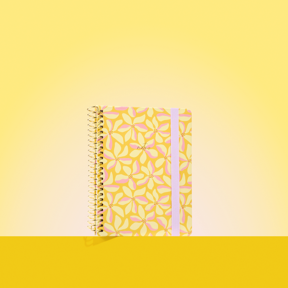 Yellow 2026 notepad with pink and cream floral pattern, gold spiral binding, and light purple elastic closure on a yellow background.