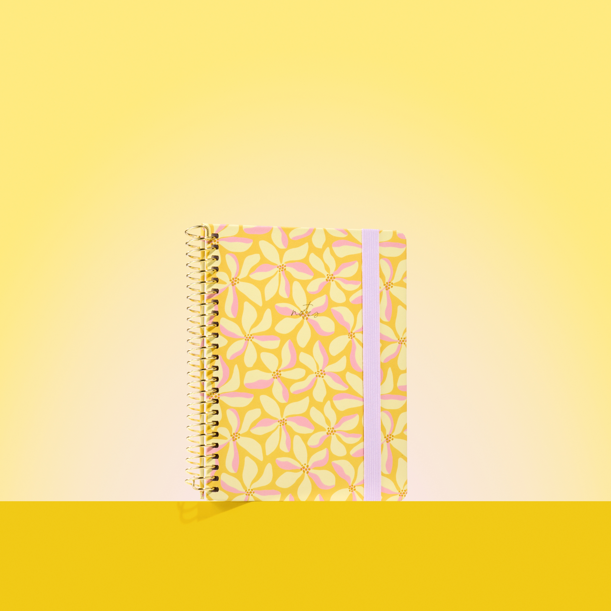 Yellow 2026 notepad with pink and cream floral pattern, gold spiral binding, and light purple elastic closure on a yellow background.