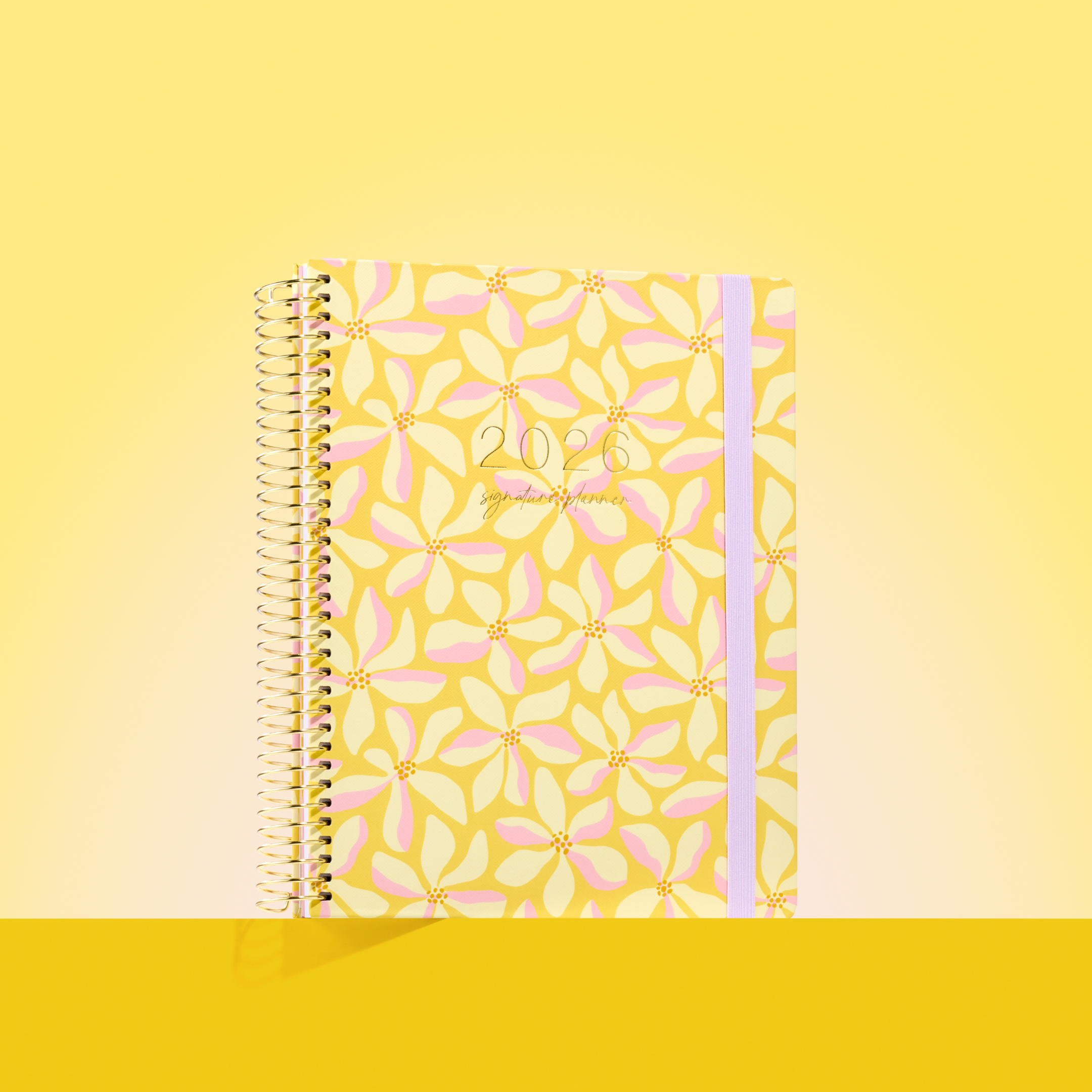 2026 planner with a pastel yellow and pink floral design, gold coil binding, and soft lavender elastic strap.