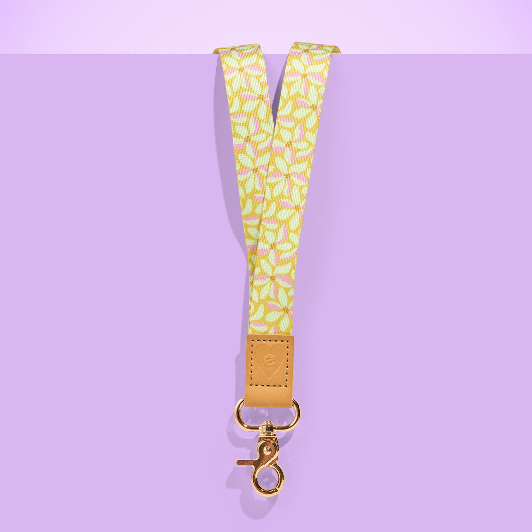 Yellow floral patterned teacher lanyard with tan leather accent and gold clasp, displayed on a purple background.