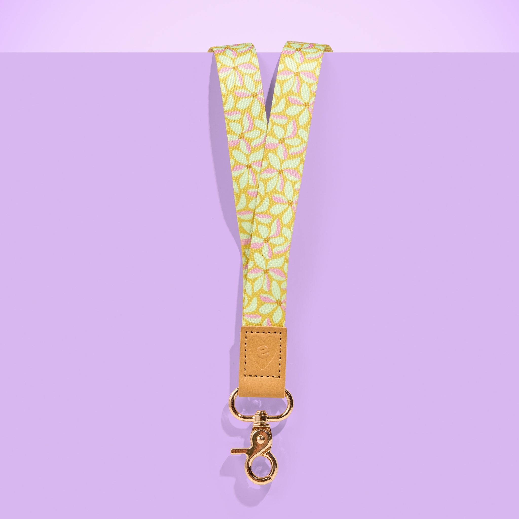 Yellow floral patterned teacher lanyard with tan leather accent and gold clasp, displayed on a purple background.