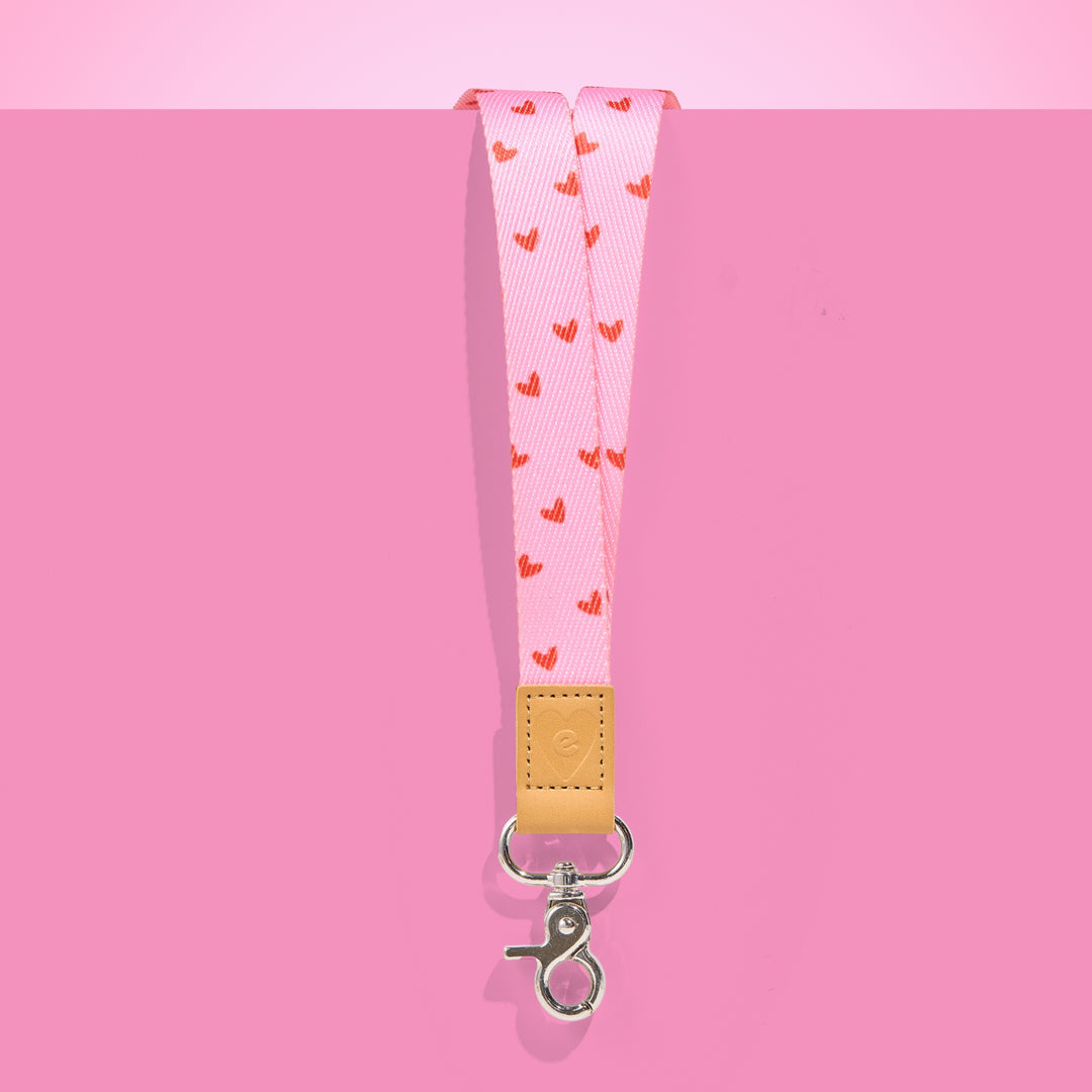 Pink teacher lanyard with red heart pattern, tan leather accent and silver clasp, displayed on a bright pink background.