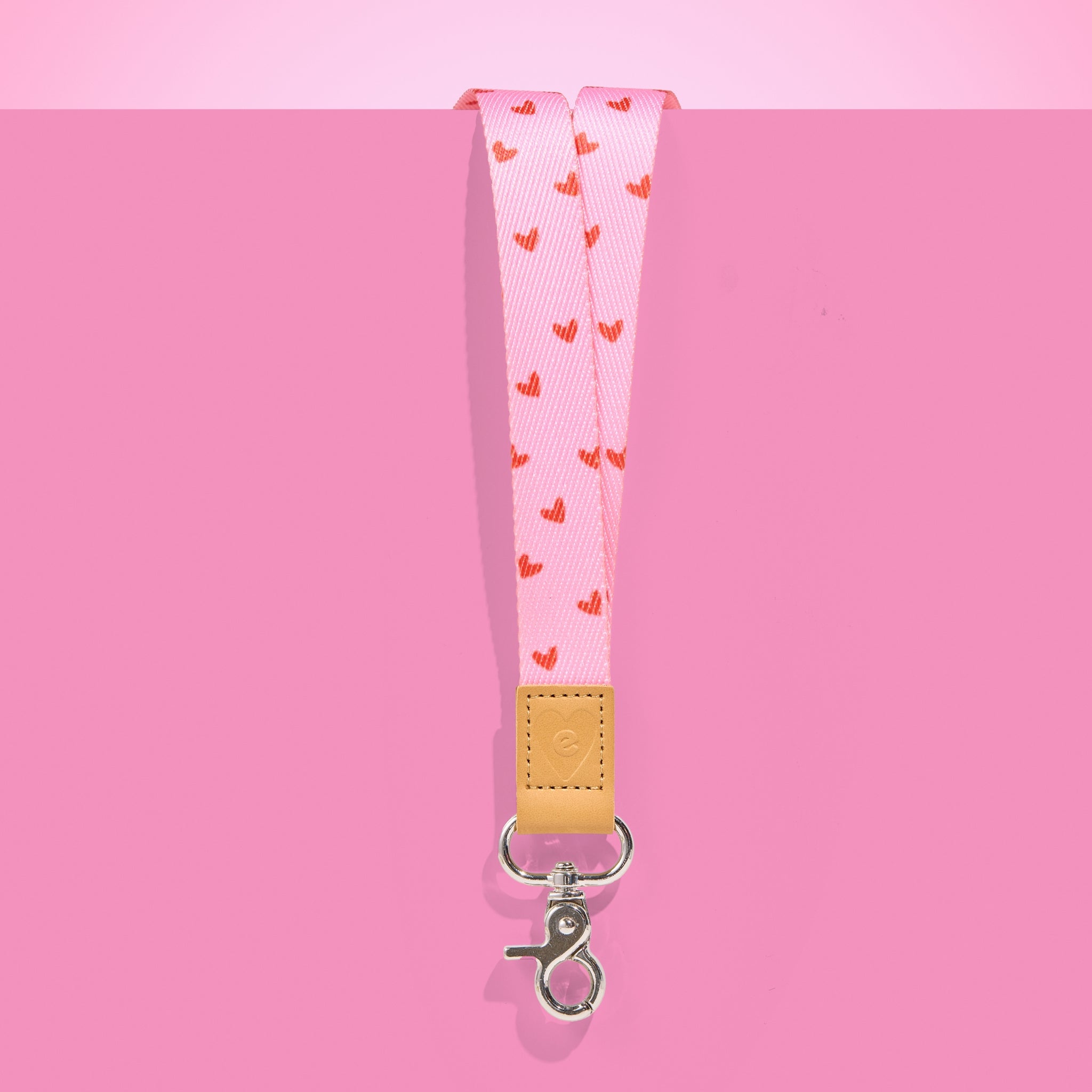 Pink teacher lanyard with red heart pattern, tan leather accent and silver clasp, displayed on a bright pink background.