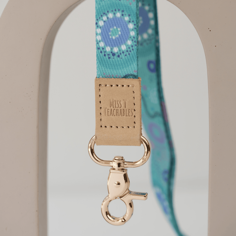 Close up of Inner Child teacher lanyard, embossed Miss T Teachables tan tab and gold swivel clasp