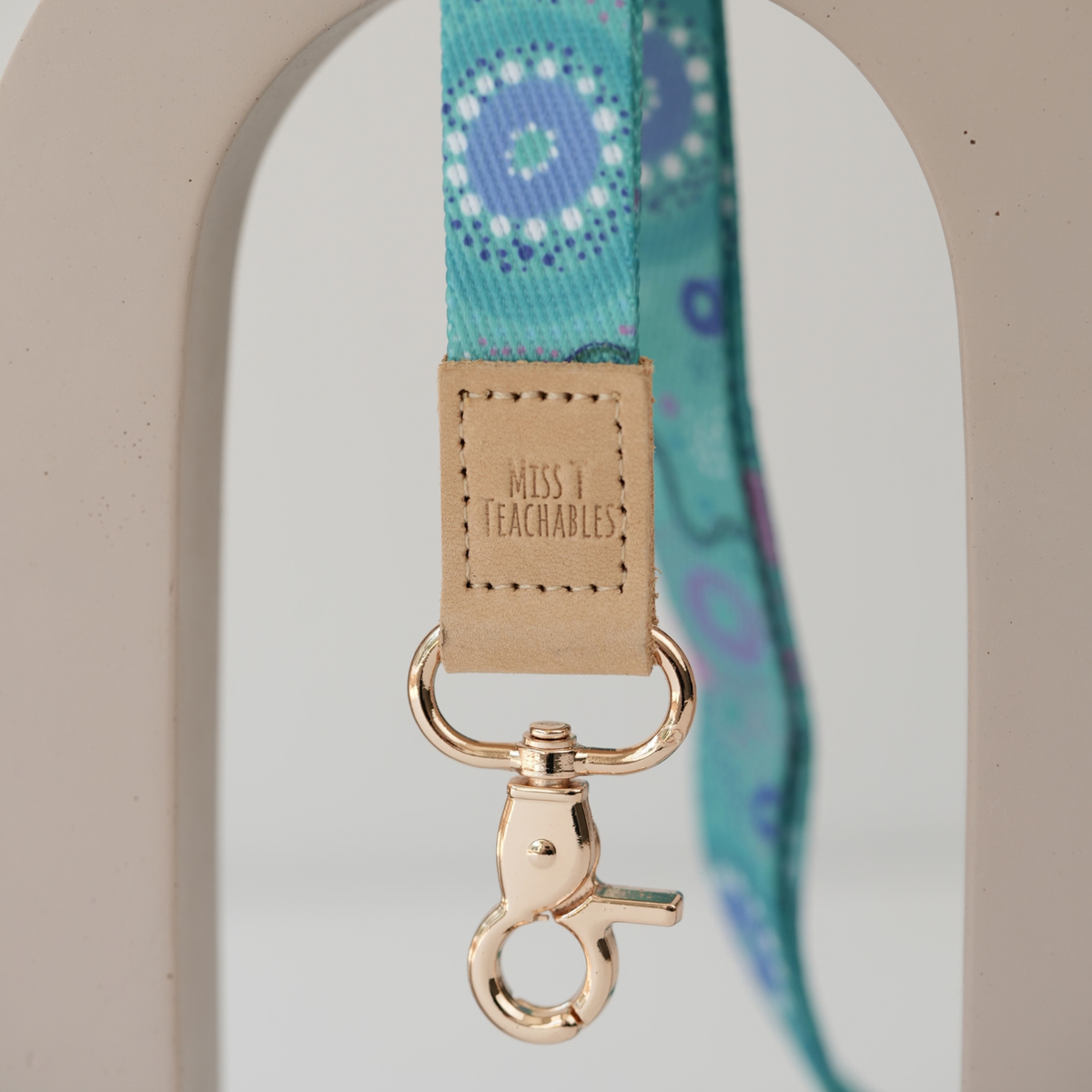 Close up of Inner Child teacher lanyard, embossed Miss T Teachables tan tab and gold swivel clasp
