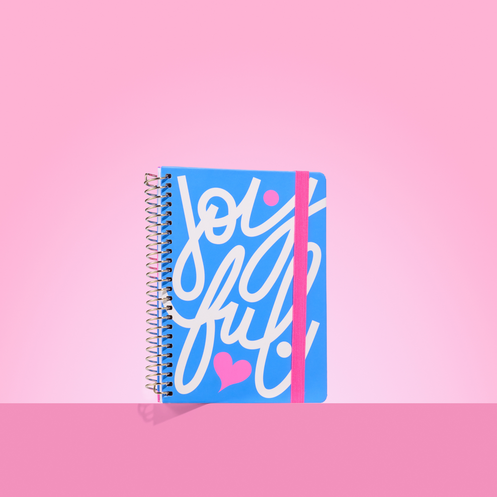 Bright blue 2026 notepad with white cursive "joyful" lettering, pink heart detail, silver spiral binding, and pink elastic closure.