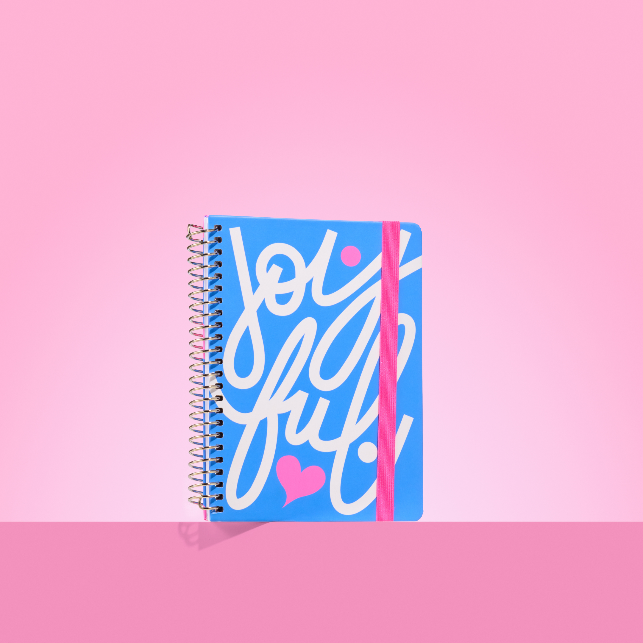 Bright blue 2026 notepad with white cursive "joyful" lettering, pink heart detail, silver spiral binding, and pink elastic closure.