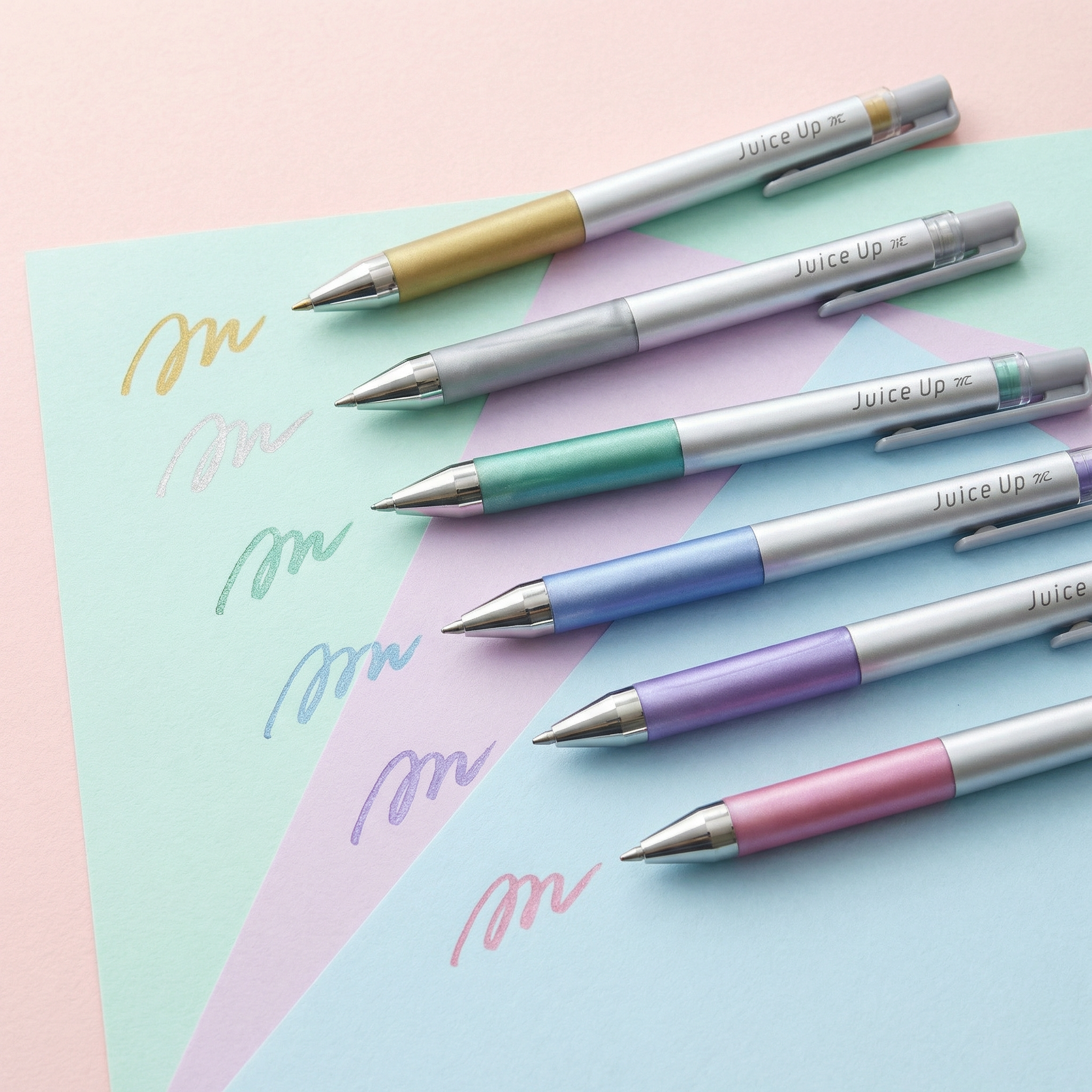 Six metallic gel pens in pastel tones (gold, silver, green, blue, purple and pink) displayed on layered pastel paper with matching shimmer ink swatches