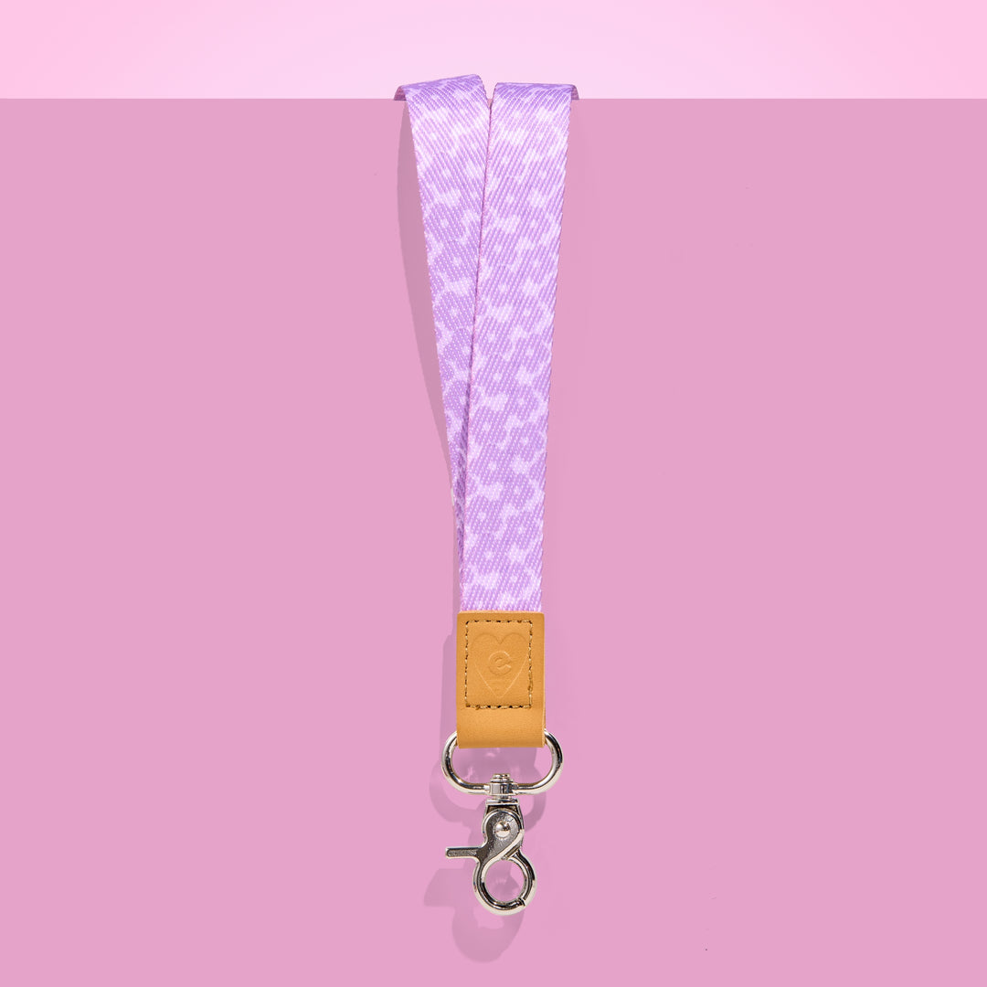 Lilac patterned teacher lanyard with tan leather accent and silver clasp, displayed on a pink background.