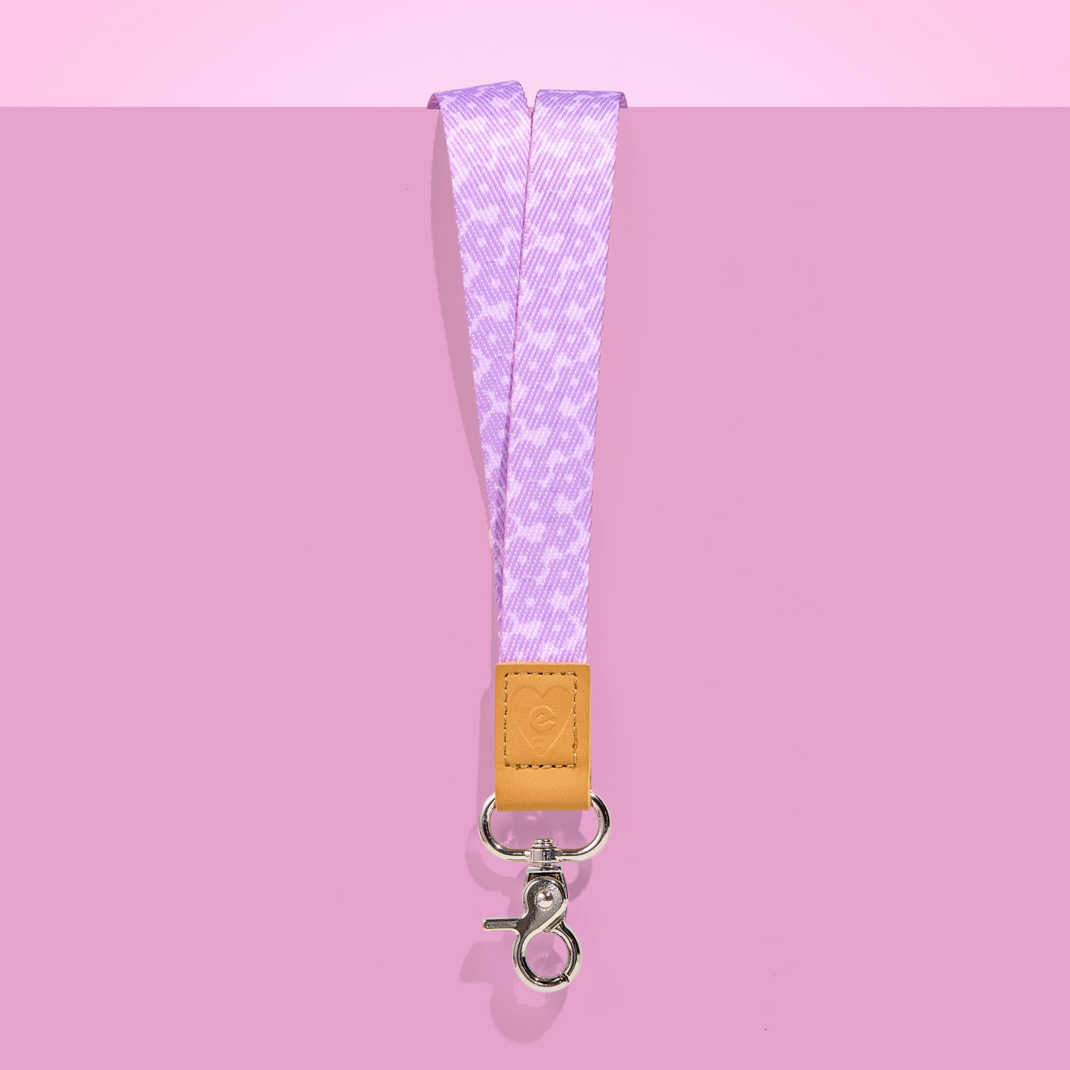 Lilac patterned teacher lanyard with tan leather accent and silver clasp, displayed on a pink background.