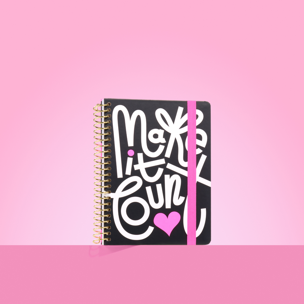 Black 2026 notepad with bold white "Make it Count" lettering, pink heart detail, gold spiral binding, and pink elastic closure.